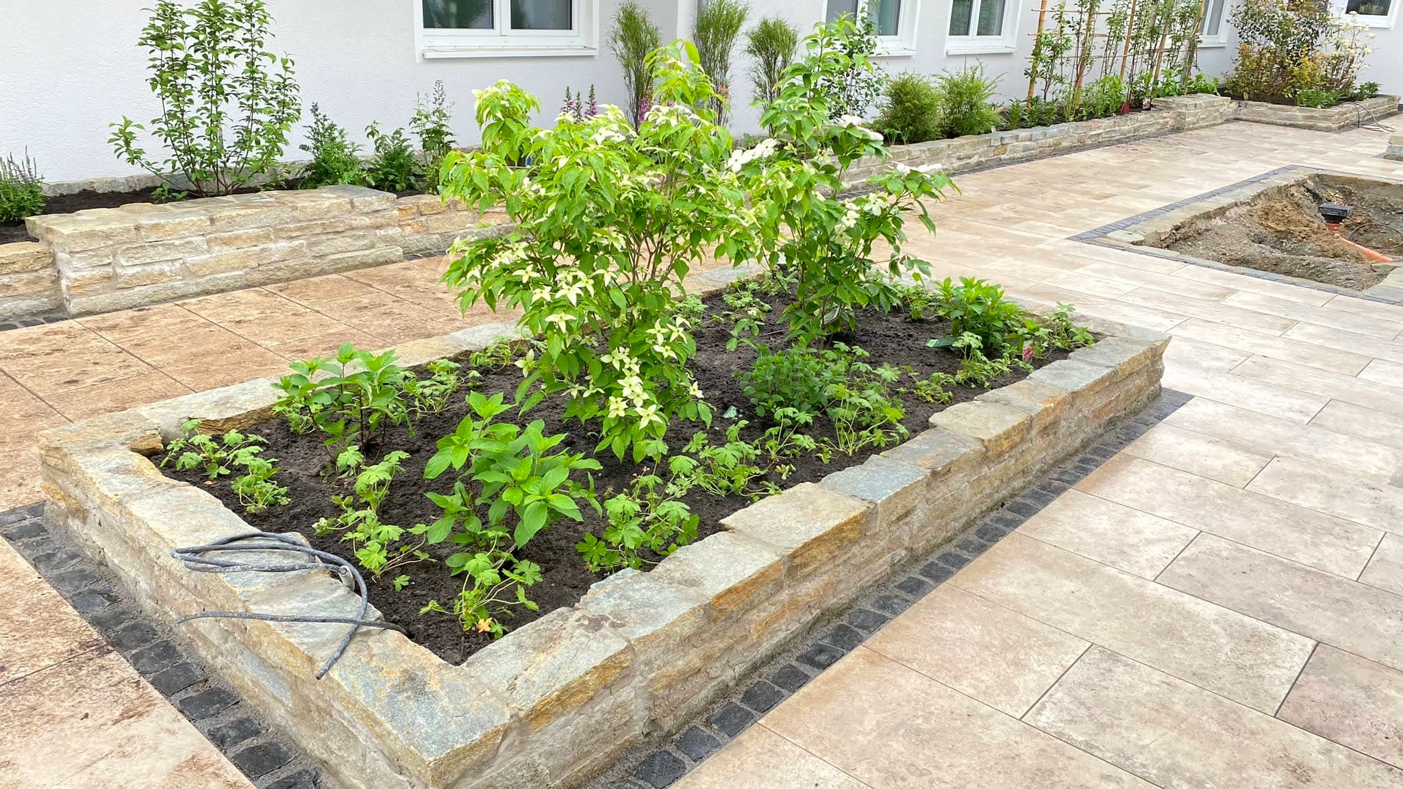 Hochbeet mit Natursteineinfassung auf einer hellen Terrasse aus Natursteinplatten