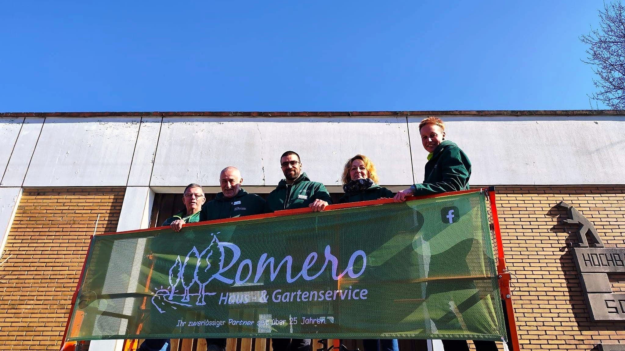 Das Team von Romero Haus- & Gartenservice auf einer Arbeitsbühne hinter dem Firmenbanner